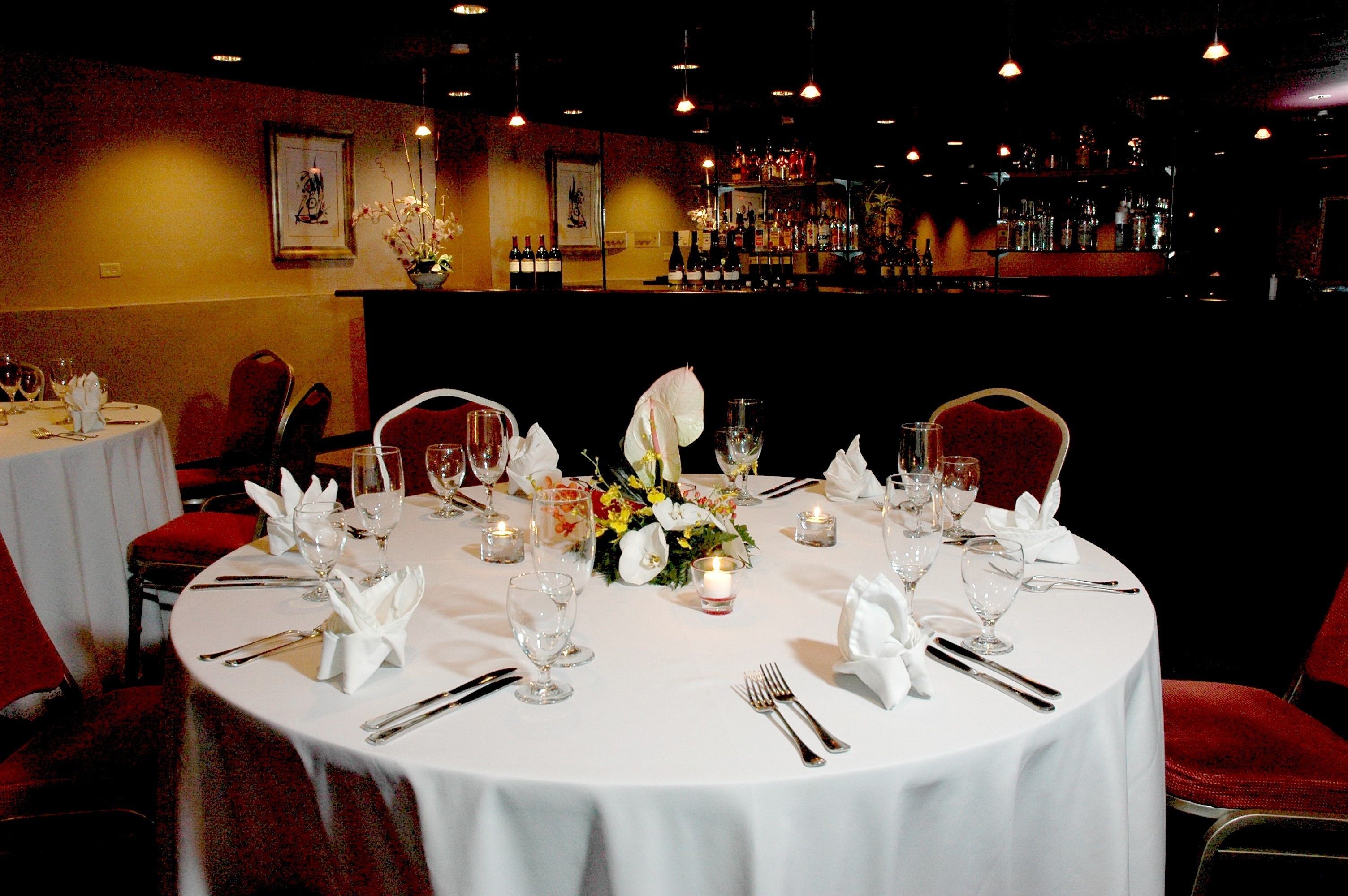 A restaurant with round tables set for dining, featuring white tablecloths, glassware, and floral centerpieces.