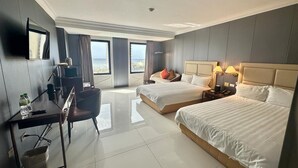Habitación de hotel con dos camas, un escritorio, una silla, un televisor y vistas al mar.