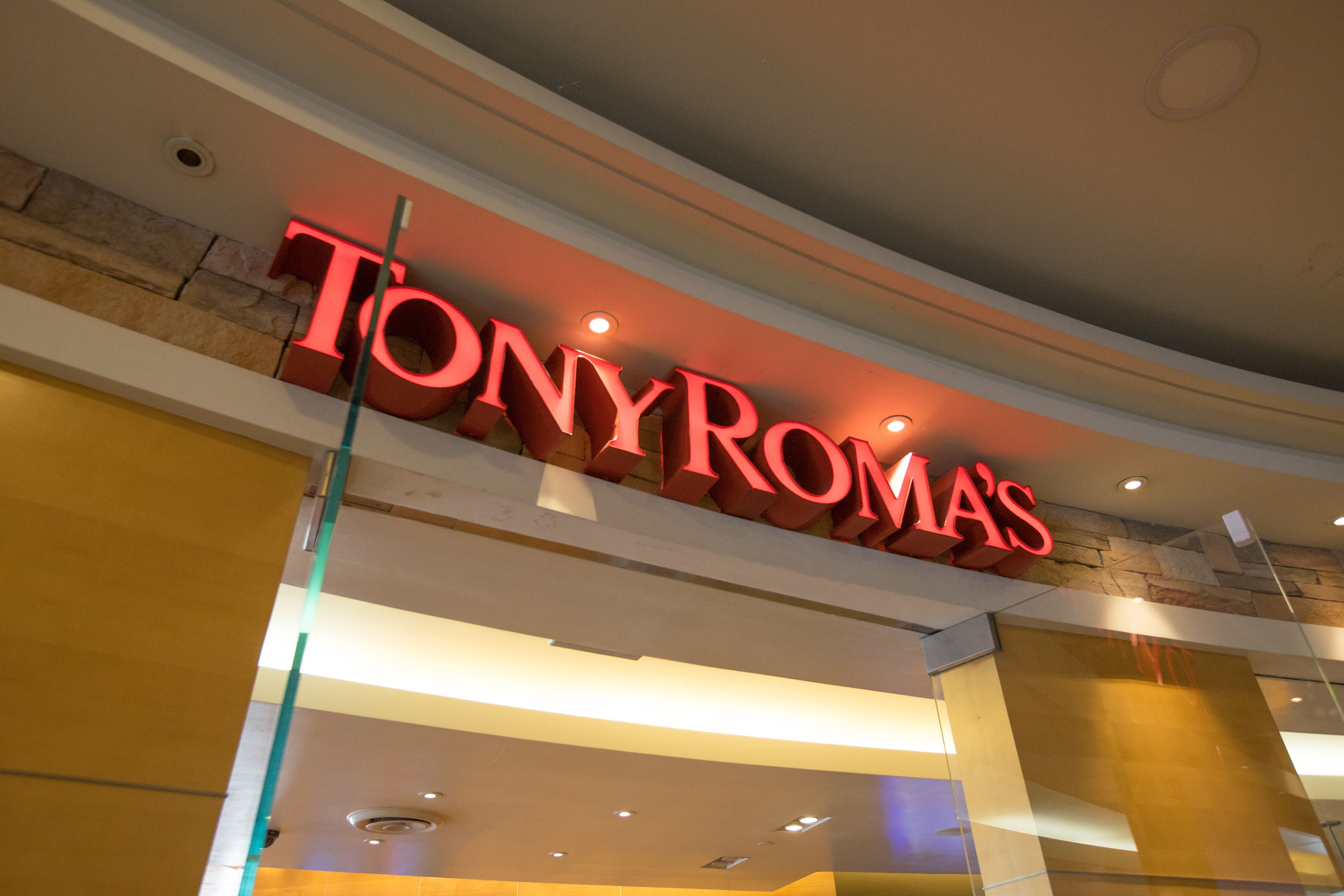 Un letrero de 'TONY ROMA'S' en un edificio moderno con detalles de piedra e iluminación empotrada.