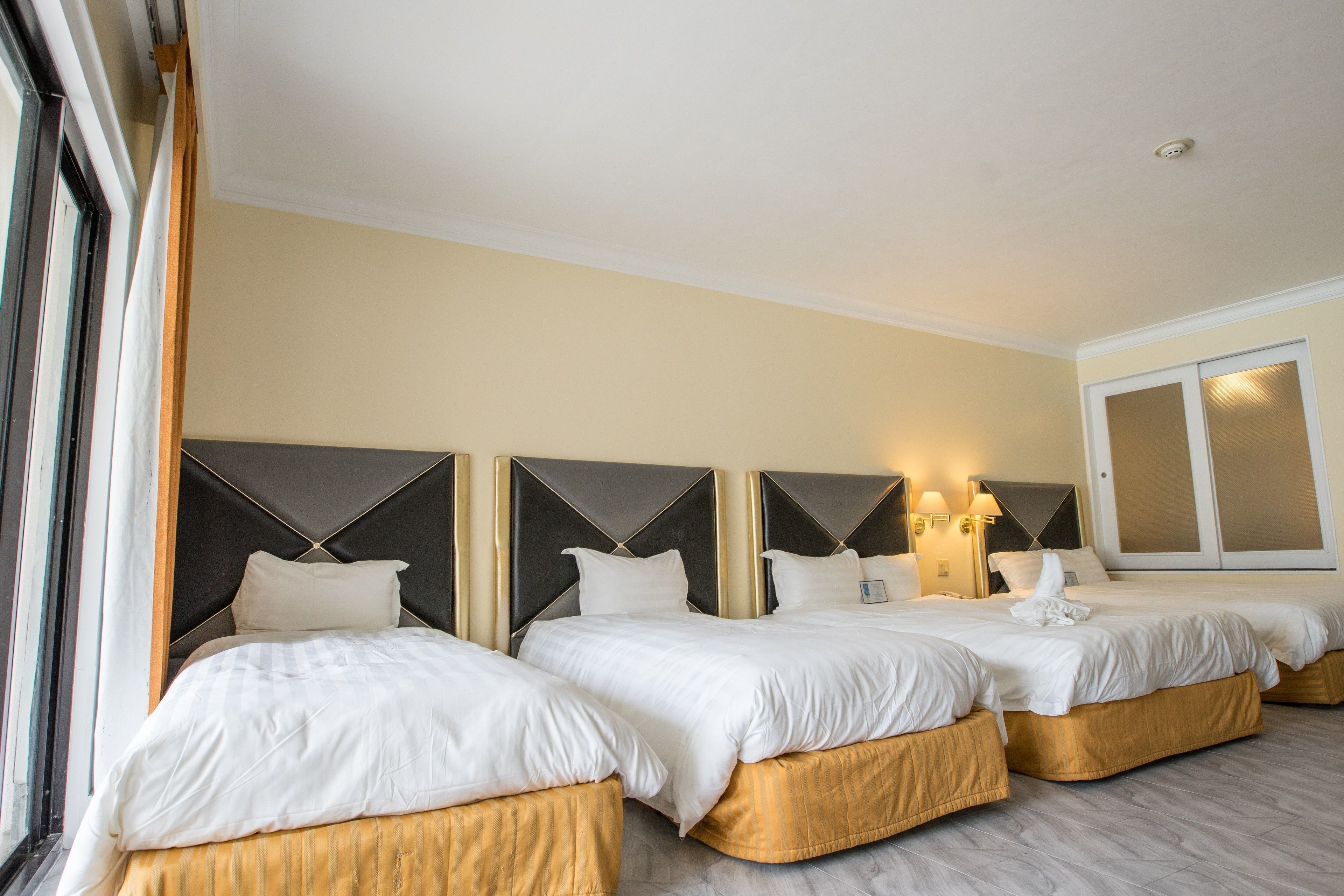 A hotel room with three beds, each with a headboard and bedside lamps.