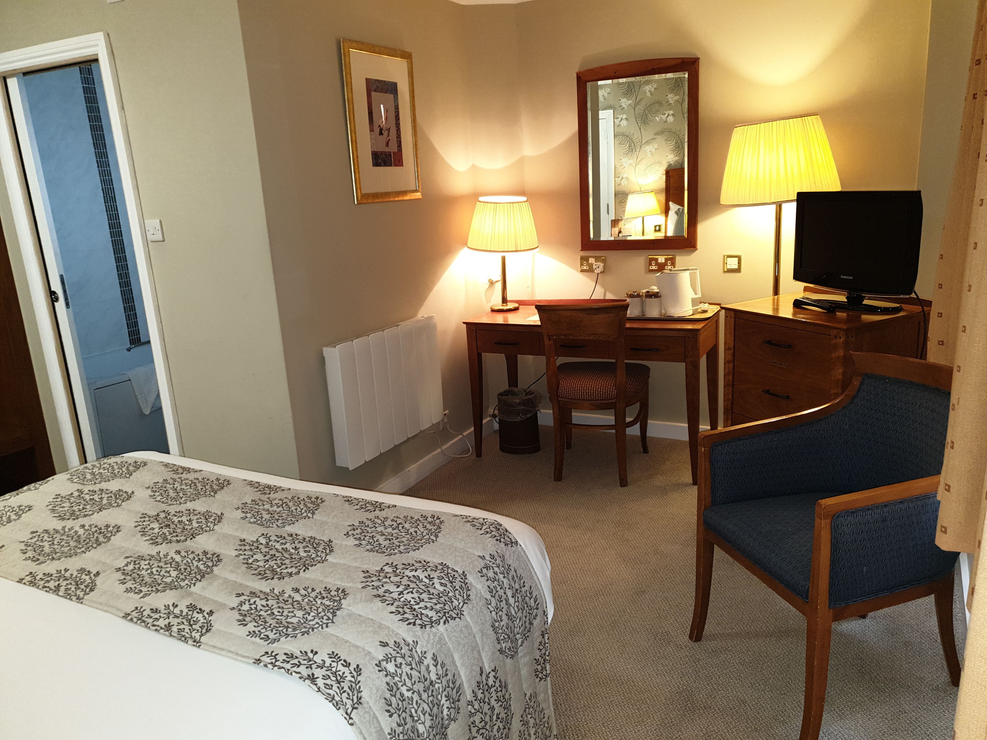A hotel room with a bed, a desk, a chair, a television, and a lamp.