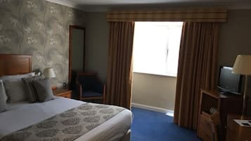 A hotel room with a large bed, a chair, a desk with a television, and a window with curtains.