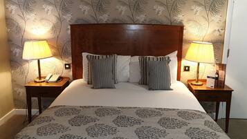 A neatly made bed with a floral-patterned bedspread, flanked by two bedside tables with lamps and a telephone.