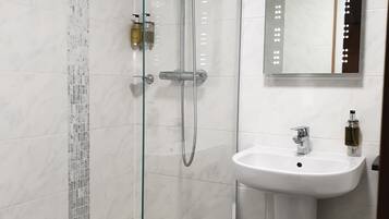 A modern bathroom with a glass-enclosed shower, a white pedestal sink, and a mirror with lights.