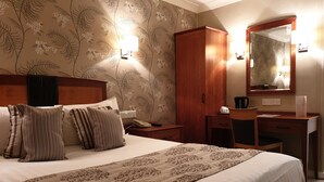 Une chambre d’hôtel comprenant un lit, un bureau, une chaise, une armoire et un miroir.