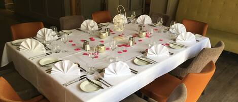 A dining table set for six with white tablecloths, orange chairs, and pink flower petals.