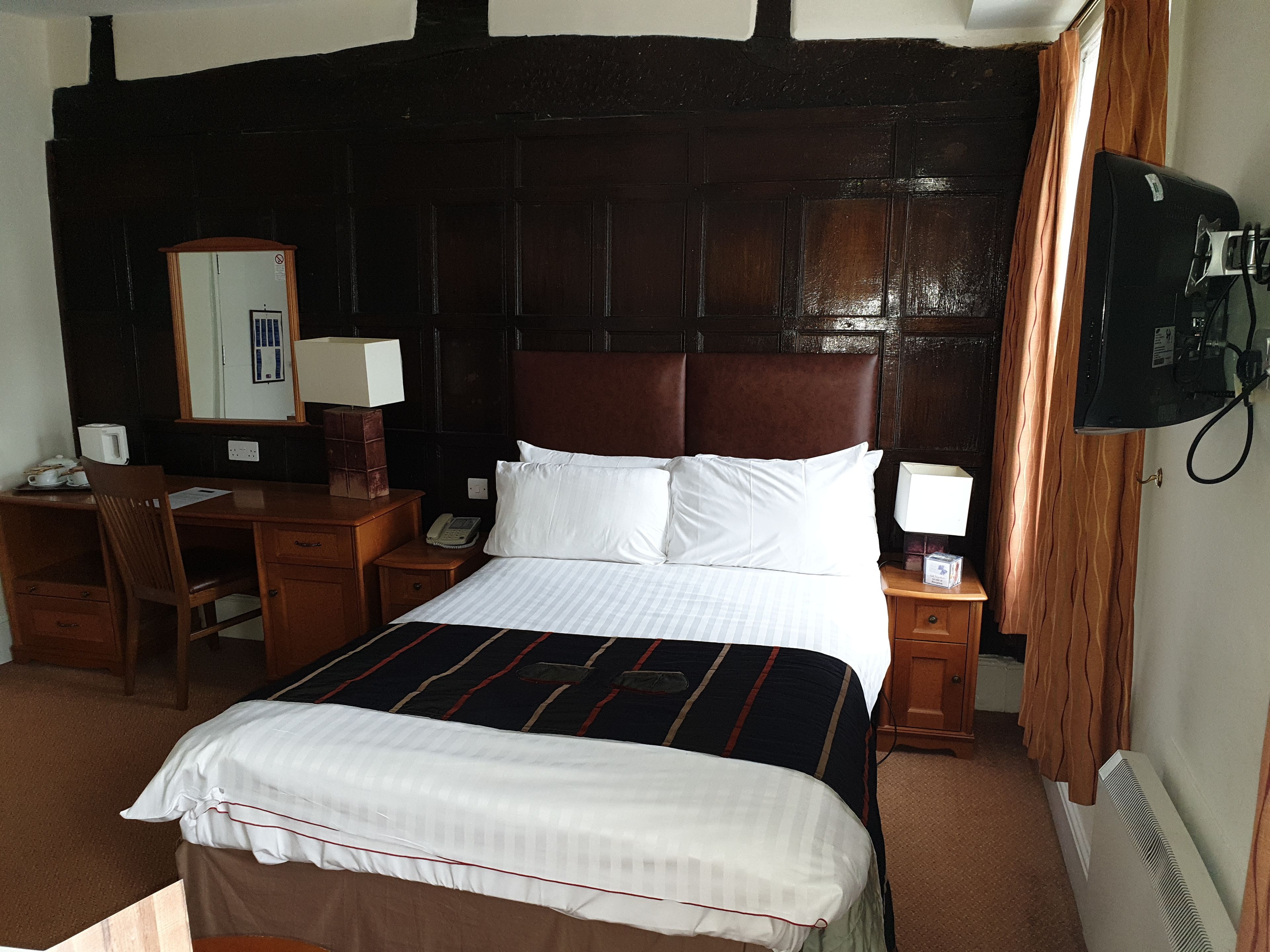 A hotel room with a large bed, a desk with a chair, a telephone, and a television on the wall.
