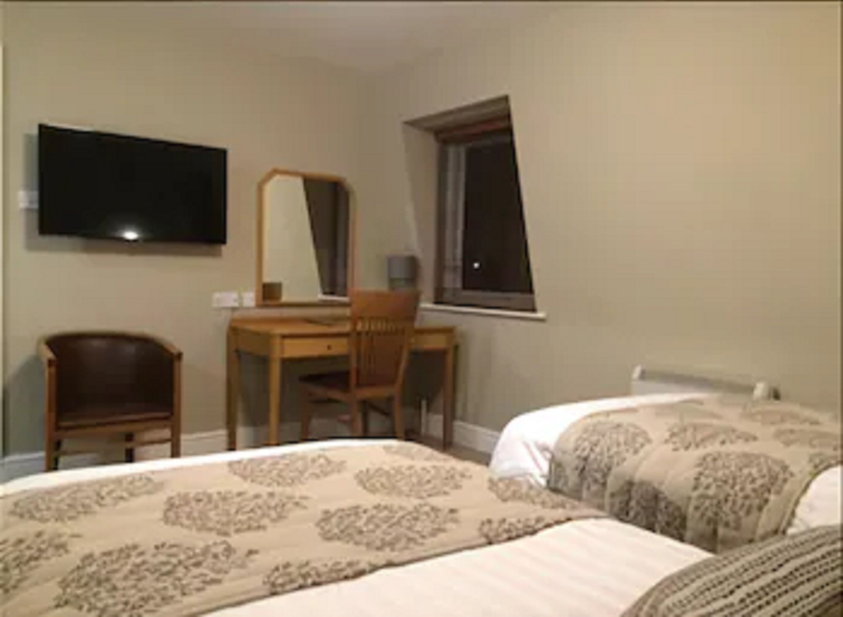 Quarto com duas camas, uma escrivaninha e uma televisão na parede.