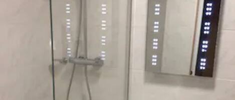 Un baño moderno con ducha acristalada, lavamanos blanco y espejo con botones iluminados.