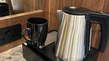 Una cocina moderna con un hervidor de acero inoxidable sobre un soporte negro, una taza negra y una encimera de mármol.