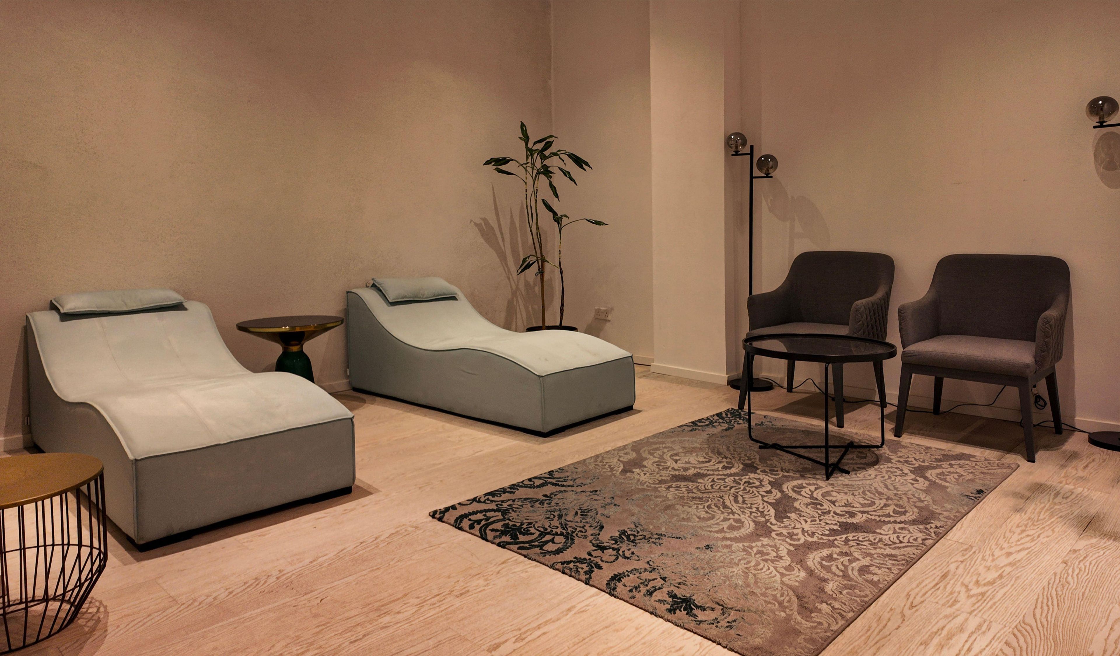 Ein stilvoller Lounge-Bereich mit zwei Sessel, einem kleinen Tisch, einer Stehlampe und einem gemusterten Teppich.