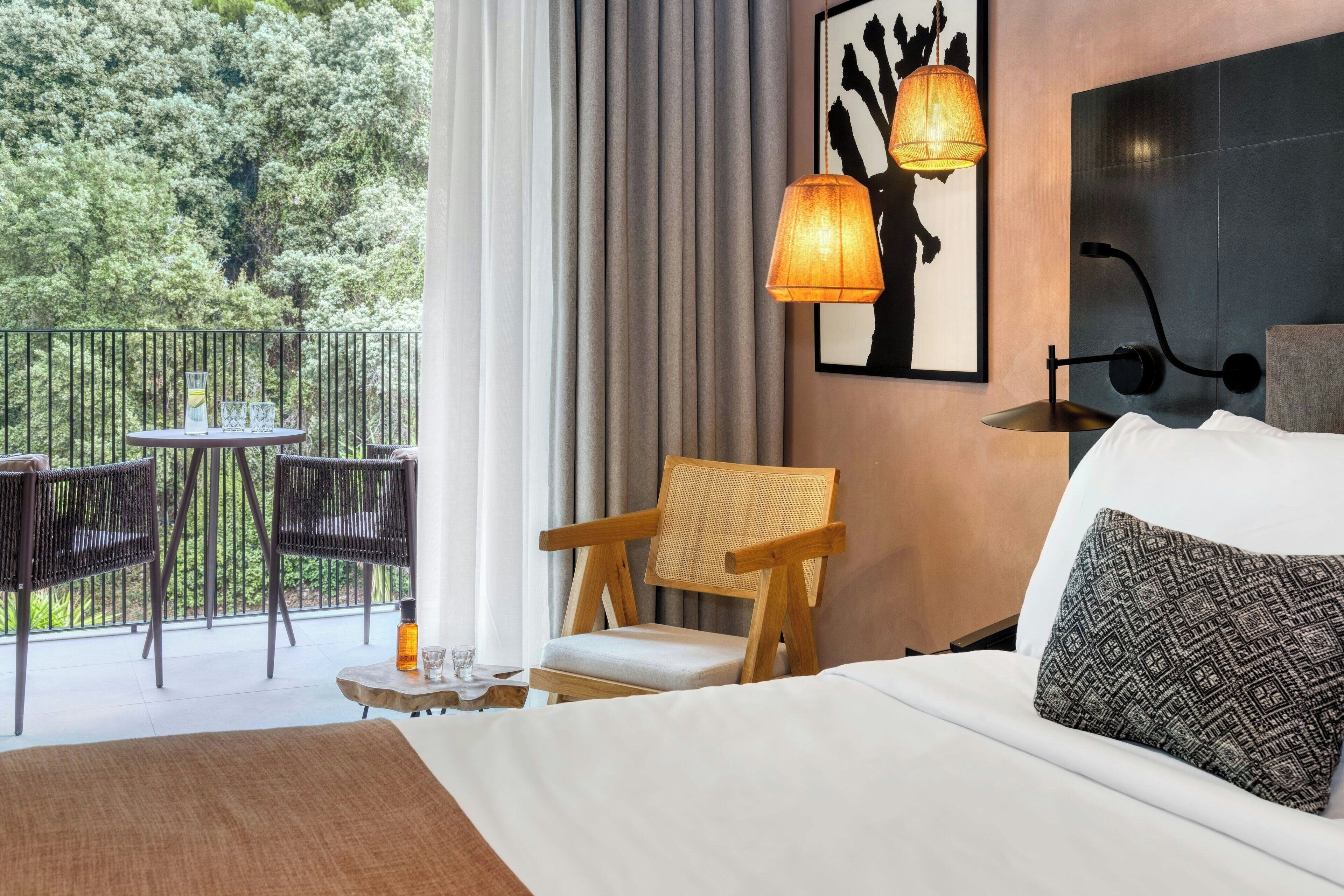 Una habitación de hotel con una cama, una silla, una mesa con un vaso y vista a zonas verdes.