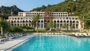 Un hotel con piscina, varios balcones y montañas al fondo.