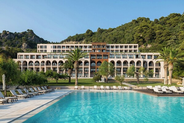 A hotel with a pool, multiple balconies, and a mountainous backdrop. - Domes of Corfu Autograph Collection (Corfu)