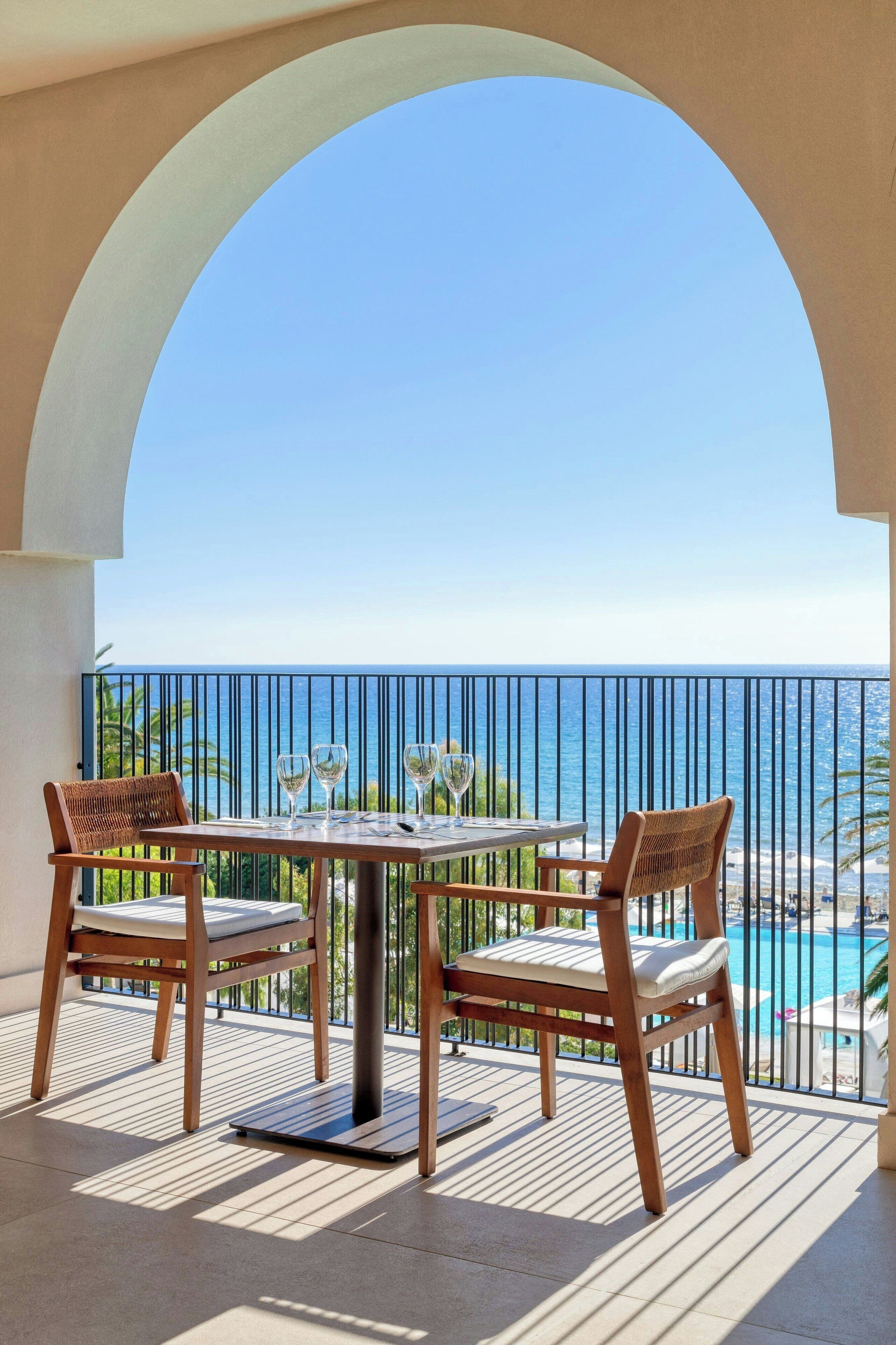 Un balcone con tavolo e sedie, vista su una piscina e l'oceano.