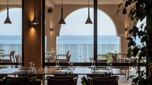Un restaurante con mesas preparadas para comer, amplias ventanas en arco y lámparas colgantes.