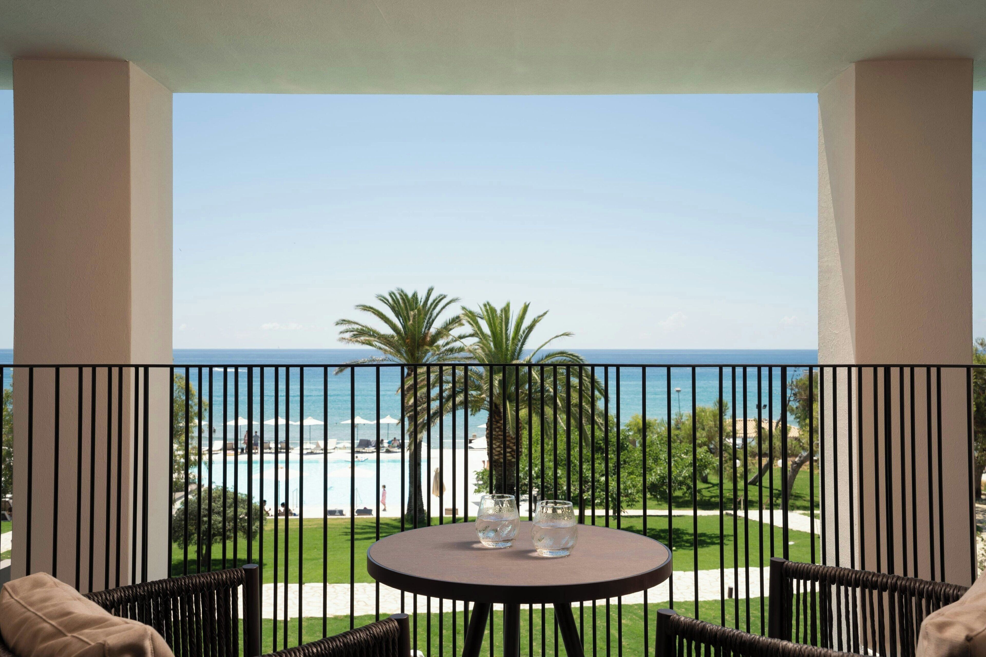 Un balcón con mesa y sillas, con vista a una playa y una piscina.