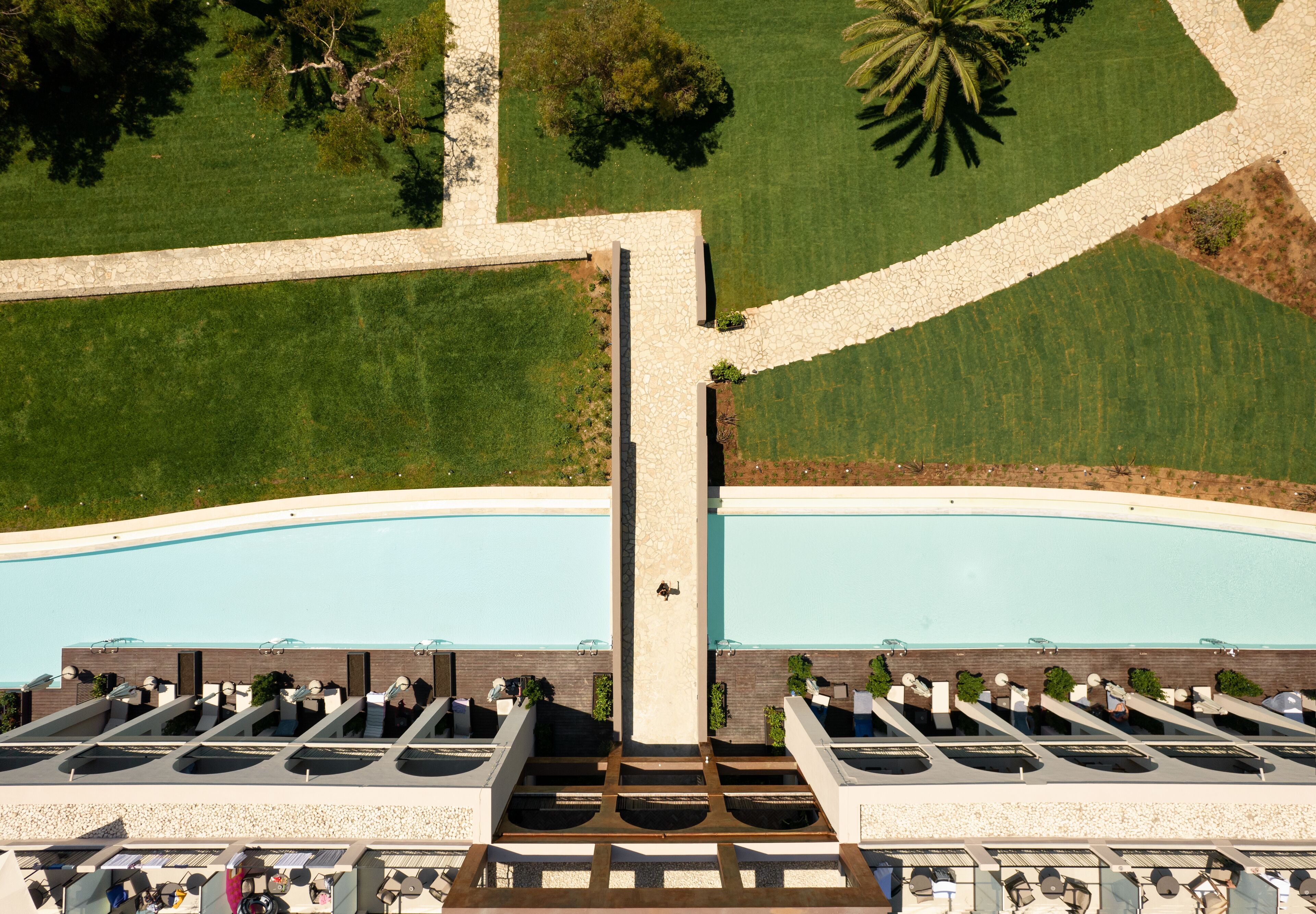 Vista aérea de un hotel con piscina, múltiples tumbonas y un camino central.