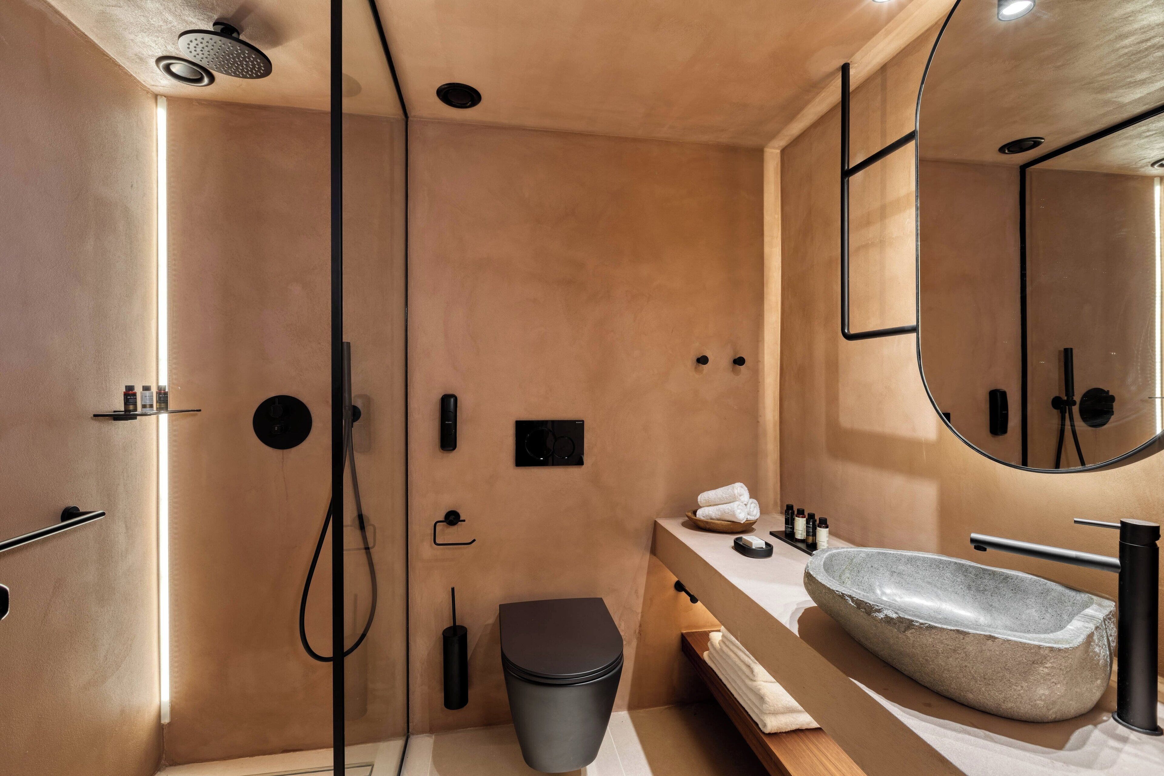 Un baño moderno con un lavamanos de piedra, un inodoro negro y una ducha con cabezal de ducha manual.