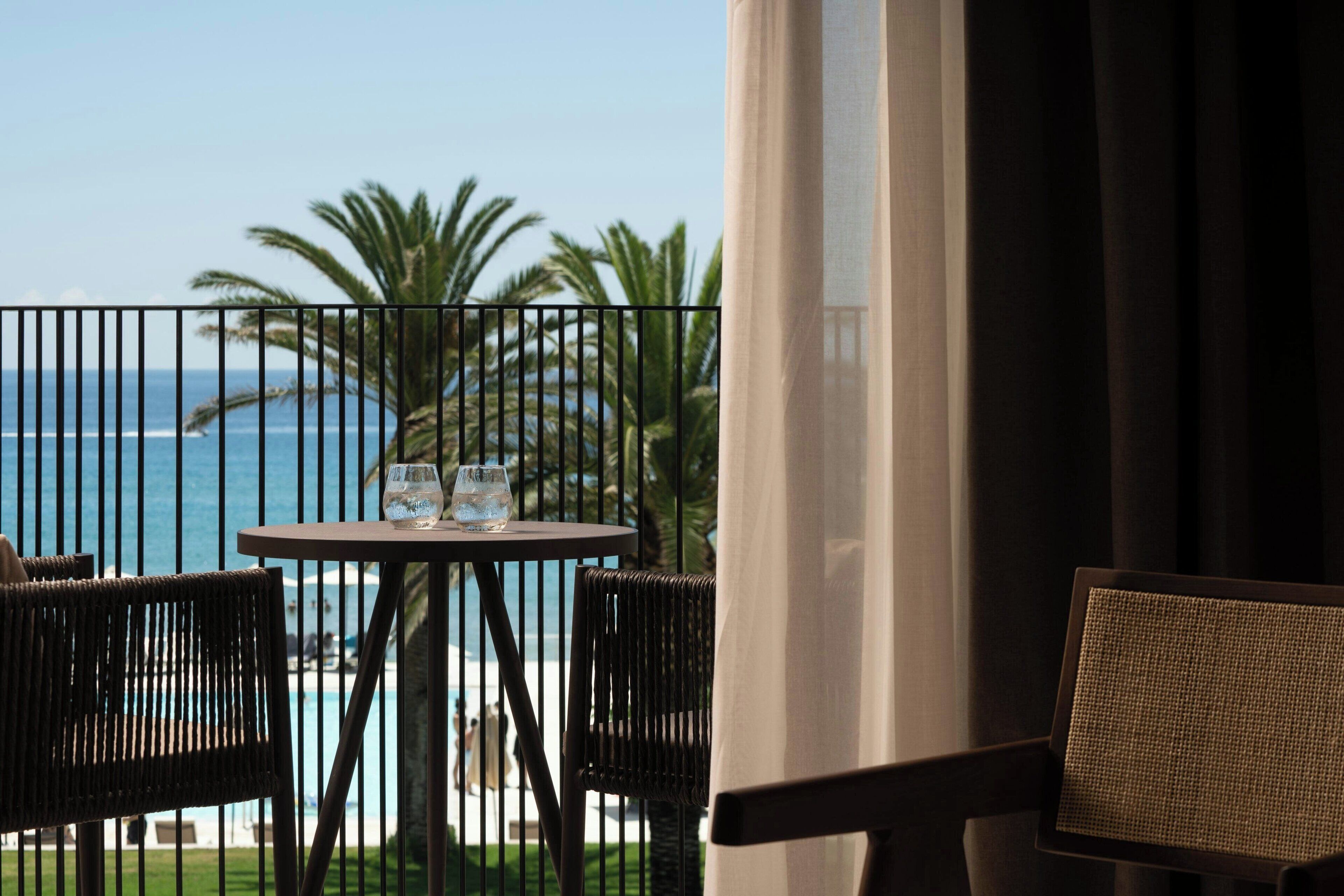 A balcony with a table and chairs, overlooking a beach and ocean.