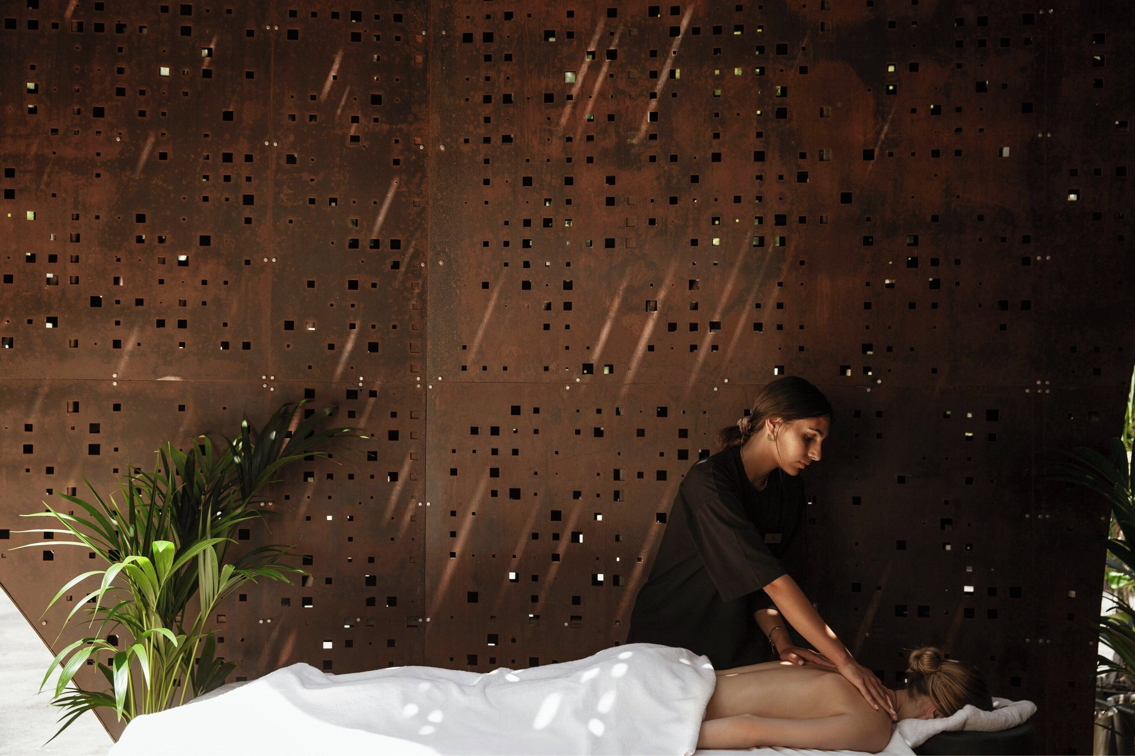 A massage therapy session in a spa setting with a perforated metal wall and potted plants.