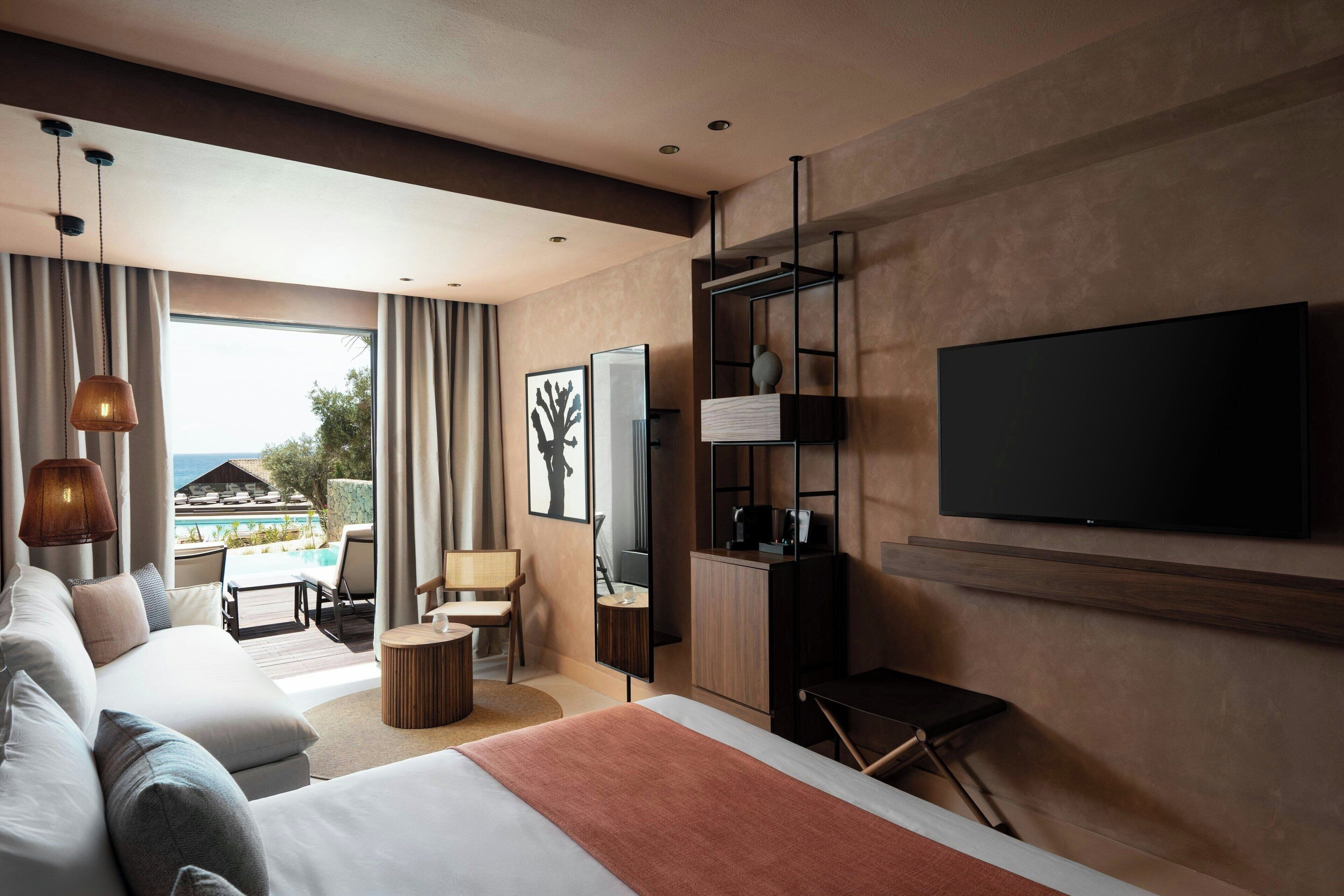 Una habitación de hotel moderna con una cama grande, un televisor montado en la pared, una zona de estar con vistas a la piscina y un balcón con cortinas.