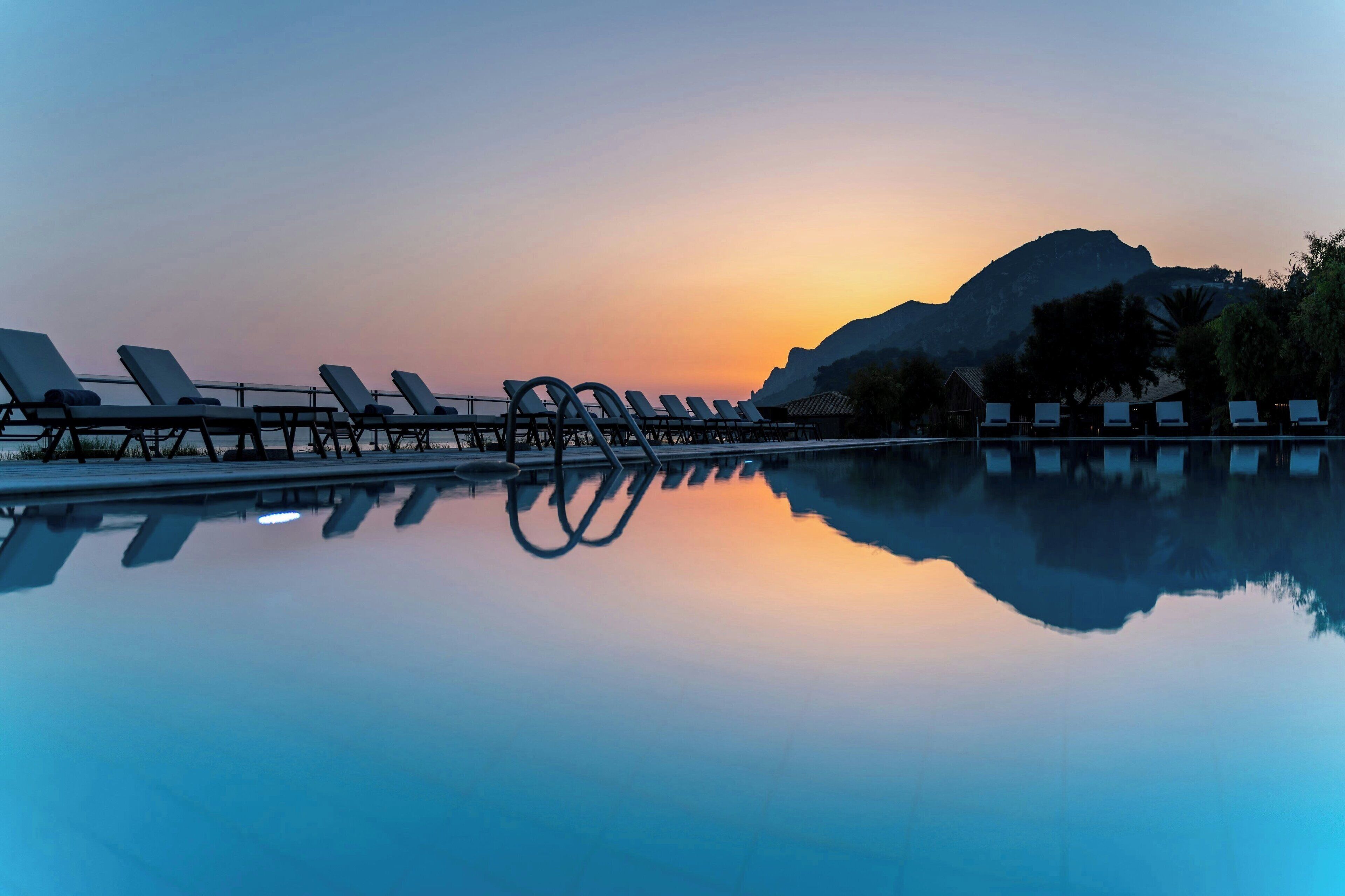 A serene poolside area with lounge chairs and a mountain backdrop during sunset.