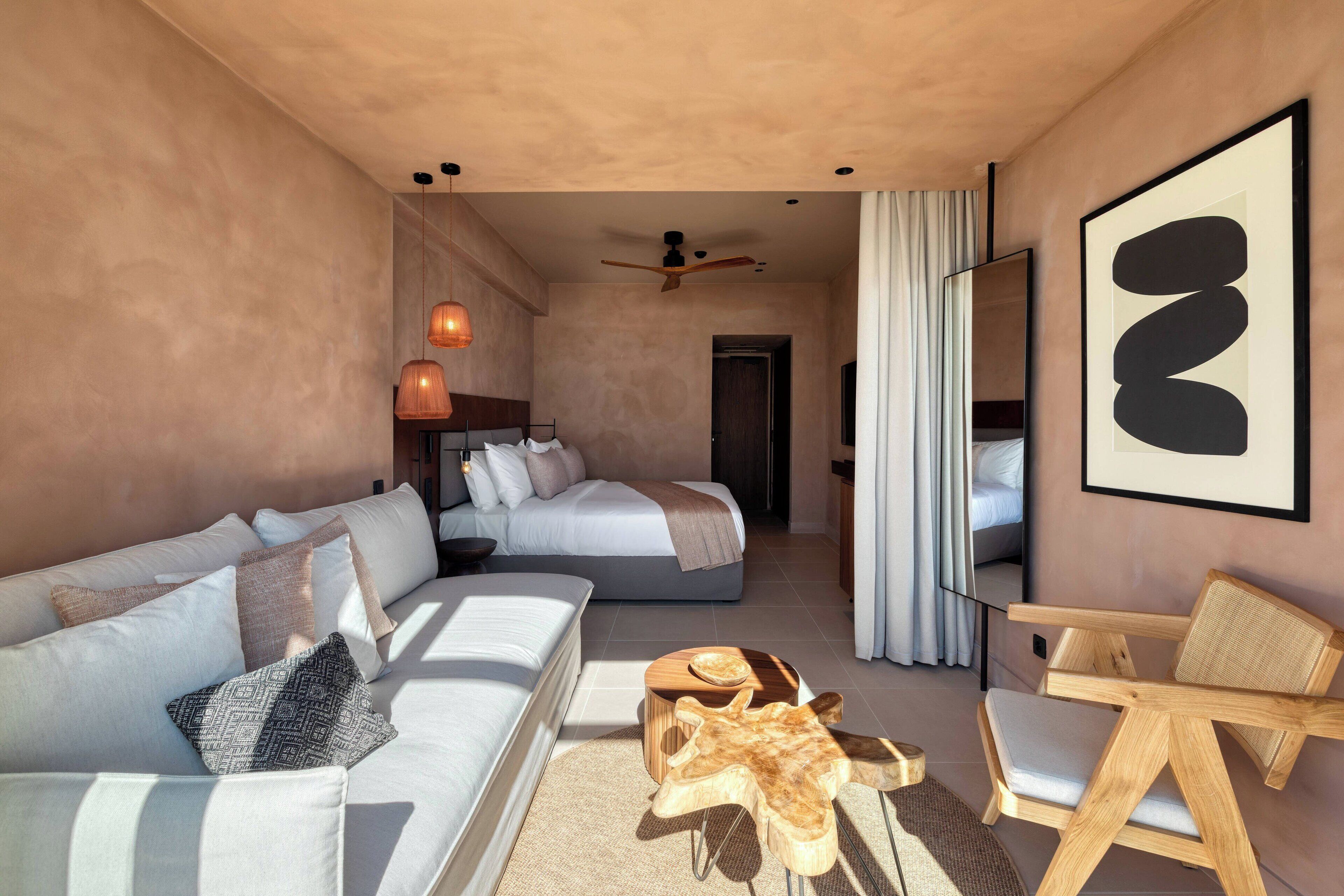 Ein modernes Hotelzimmer mit einem großen Bett, einer Couch, einem Holzstuhl und einem Deckenventilator.