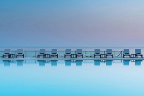 Una piscina con sillones de descanso alineados a lo largo de su borde, con vistas a un mar tranquilo.