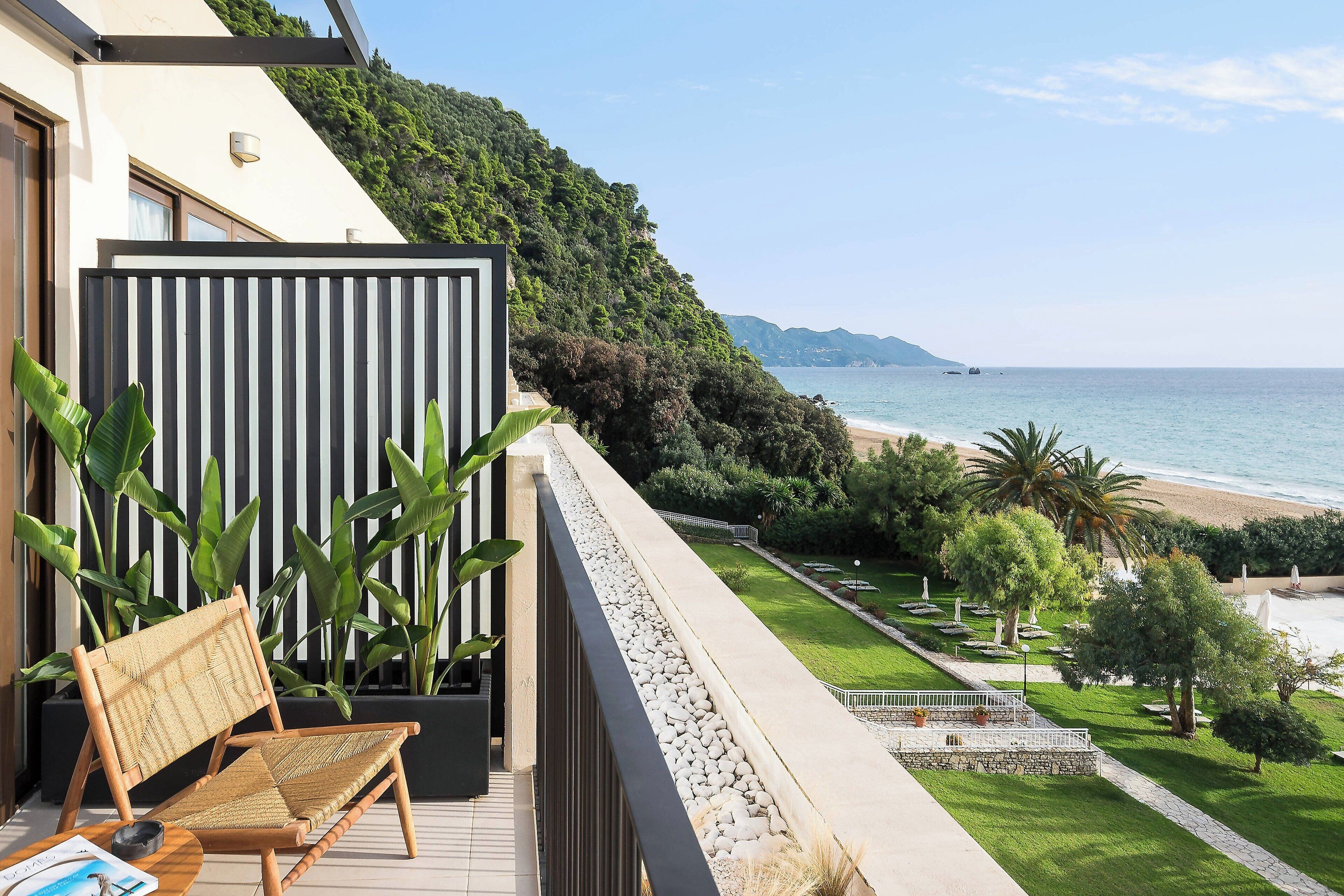 A balcony with a wicker chair, a potted plant, and a view of the beach and ocean.