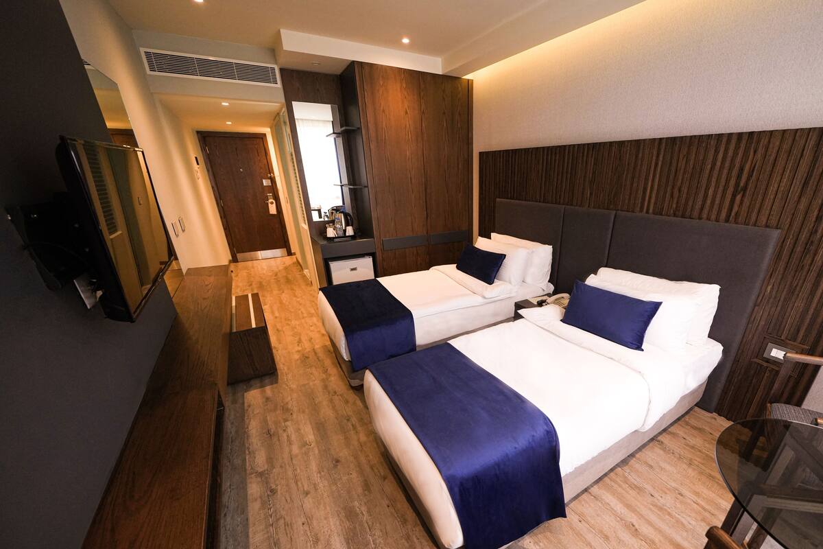 A hotel room with two beds, a desk, a mirror, and a television.