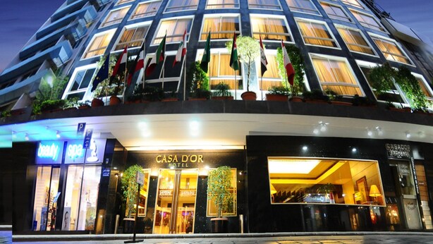 A modern hotel with a glass facade, multiple flags, and a well-lit entrance. - Casa D Or Hotel (Beirut)