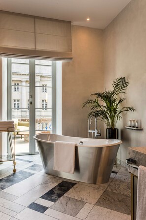 A modern bathroom with a freestanding bathtub, a potted plant, and a view of the city through large windows.