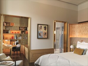 A modern hotel room with a large bed, a desk with a chair, a bookshelf, and a framed artwork on the wall.