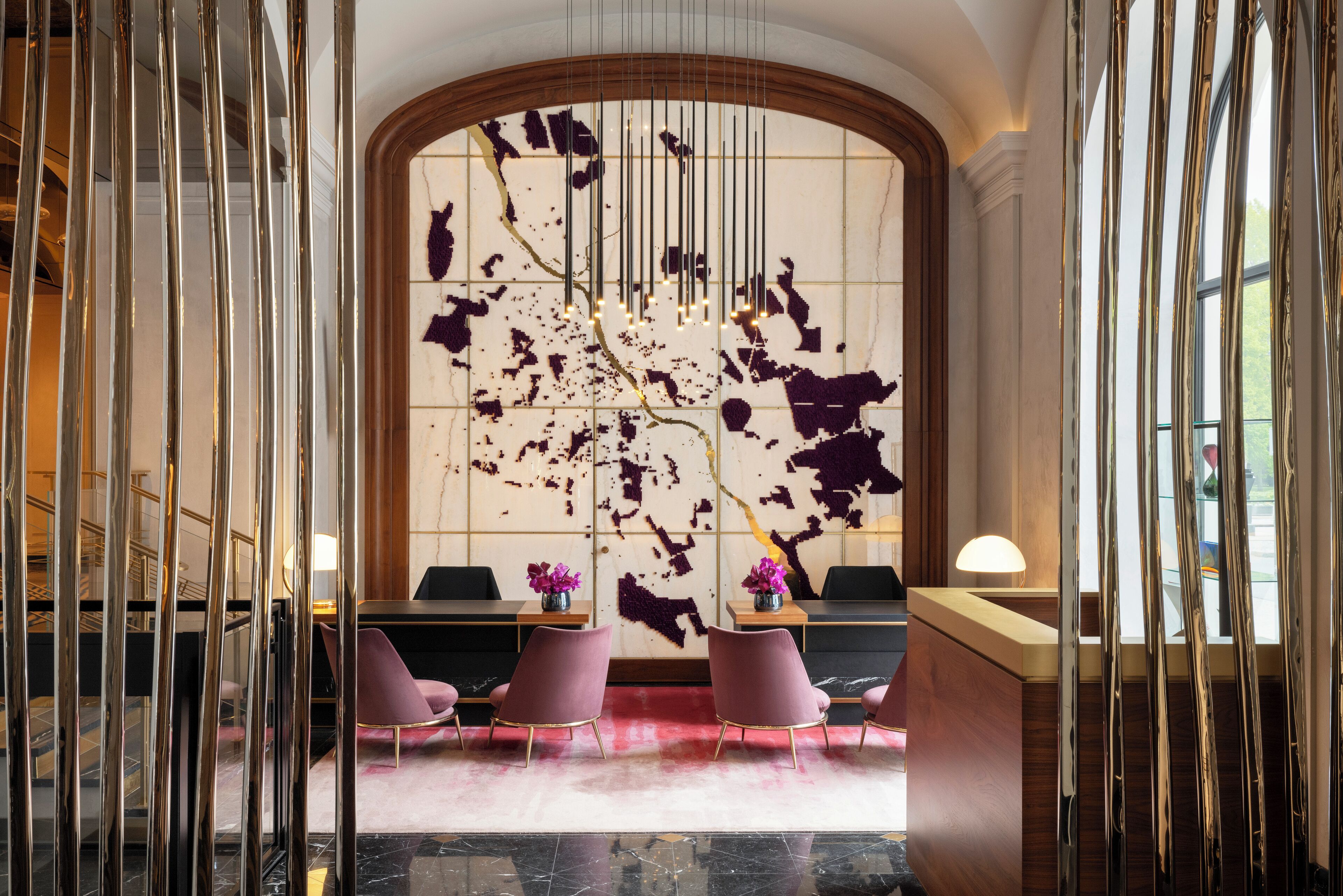 A reception area with a marble wall, a wooden reception desk, and pink chairs.