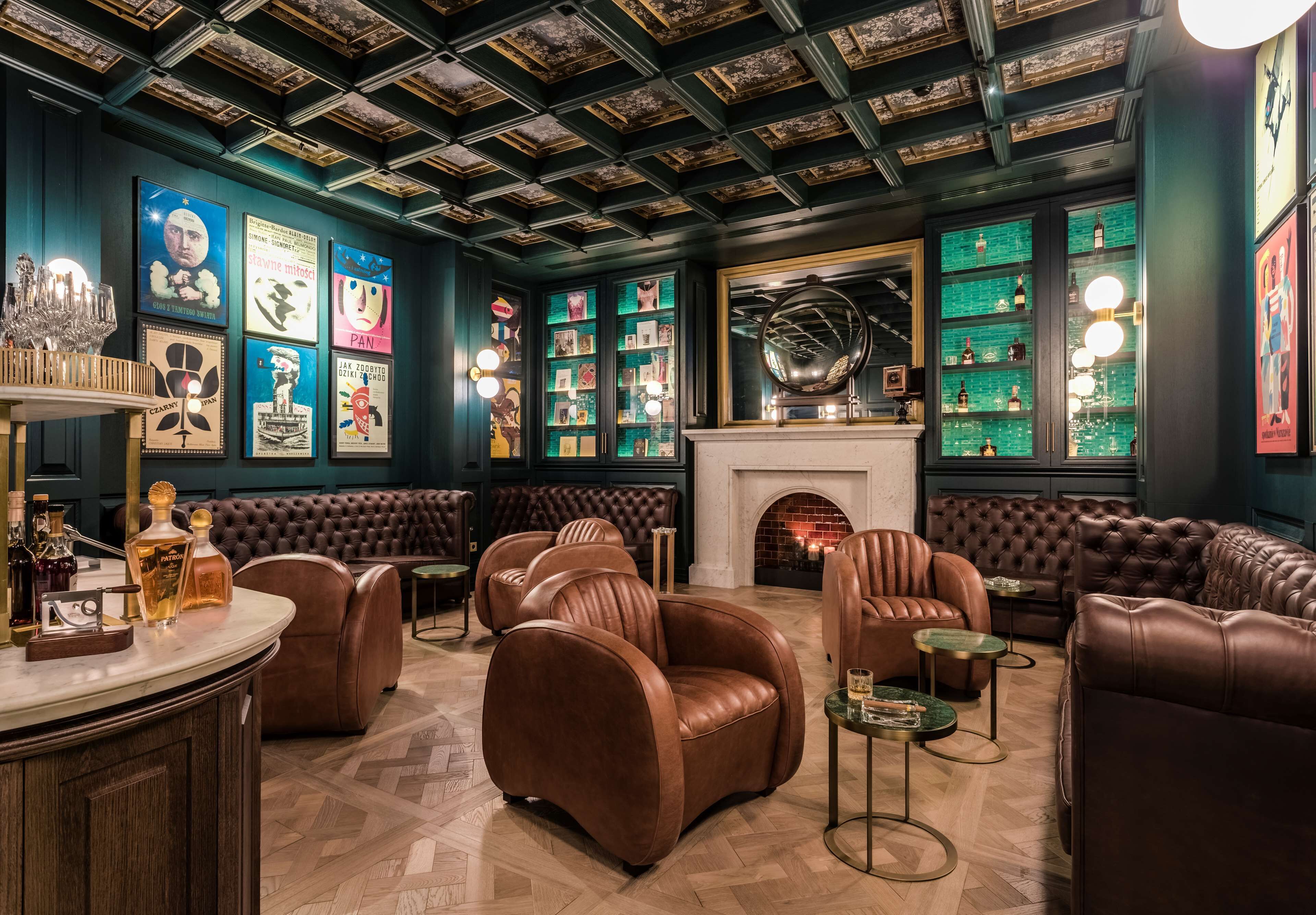 A luxurious lounge with leather sofas, a fireplace, and a wall adorned with framed posters and a globe.