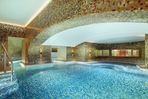 A luxurious indoor pool with mosaic walls and a clear blue pool floor.