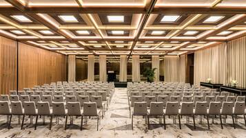 Une salle de conférence avec des rangées de chaises, un mur recouvert de panneaux en bois et un plafond doté d’un éclairage encastré.