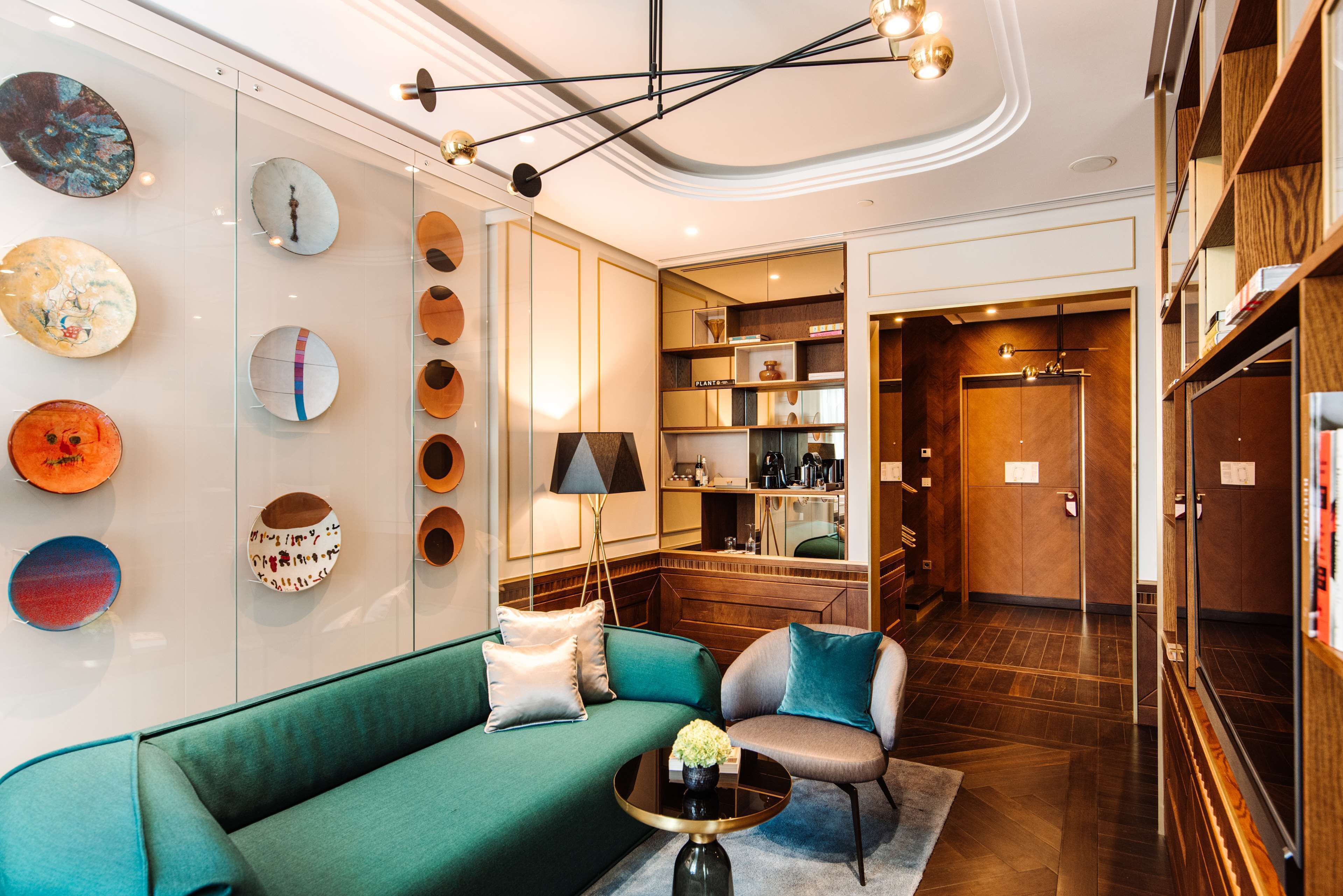 Un interior moderno con un sofá verde, dos sillones, una mesa de centro y una pared decorada con piezas de arte circulares.