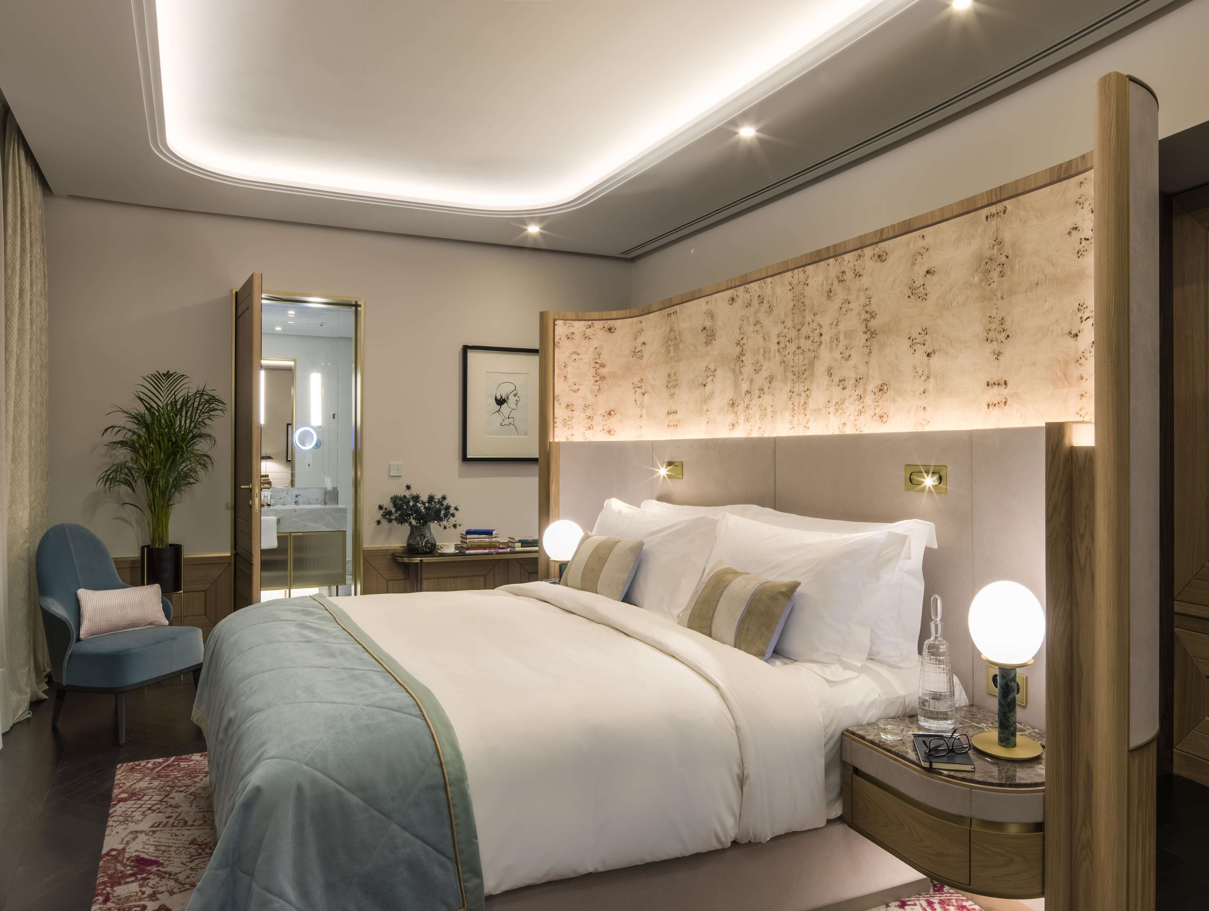 A modern hotel bedroom with a large bed, bedside tables with lamps, a mirror, and a potted plant.