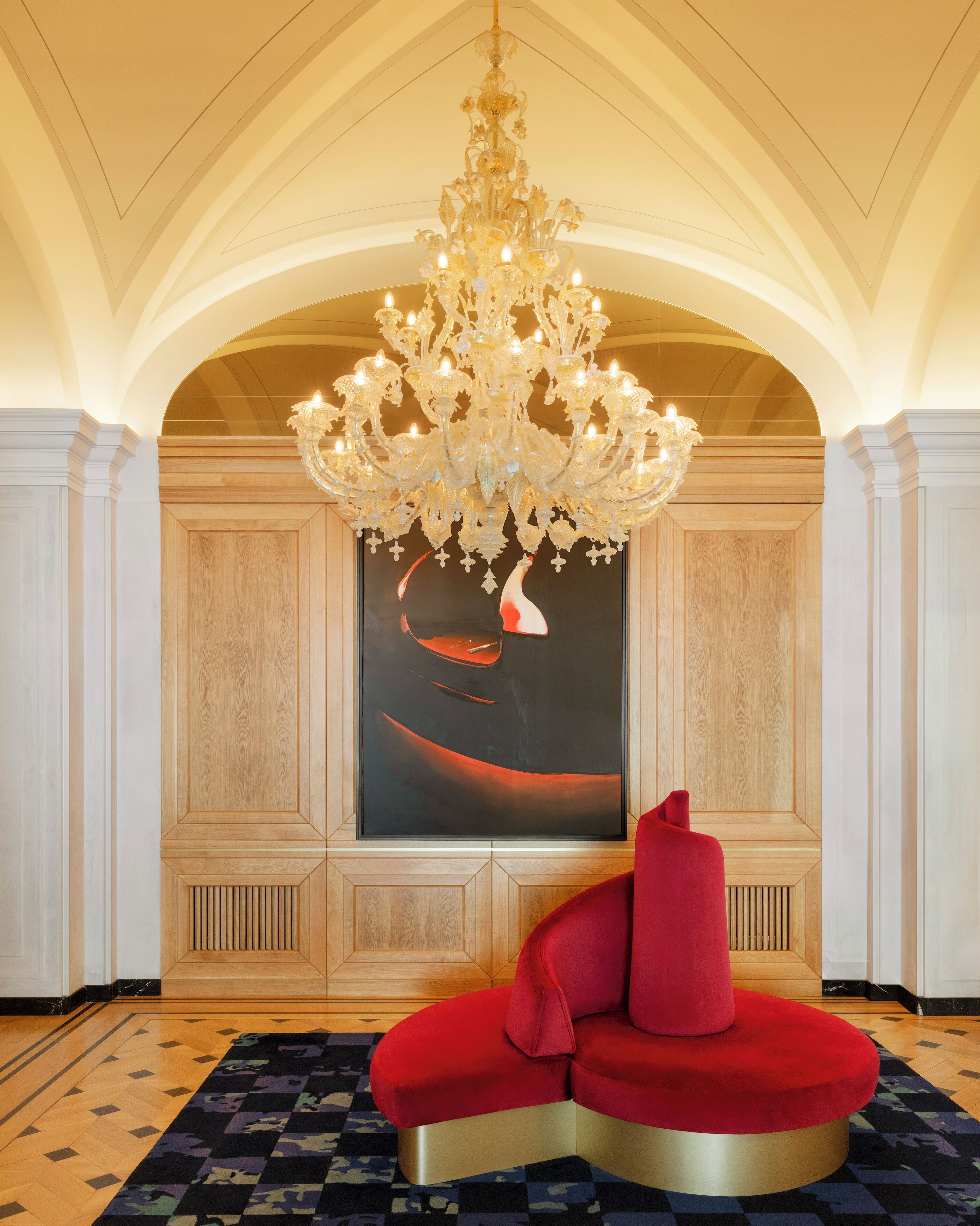 Un hall d’entrée agrémenté d’un grand lustre, d’un espace détente aux fauteuils rouges et d’un grand tableau abstrait accroché au mur.