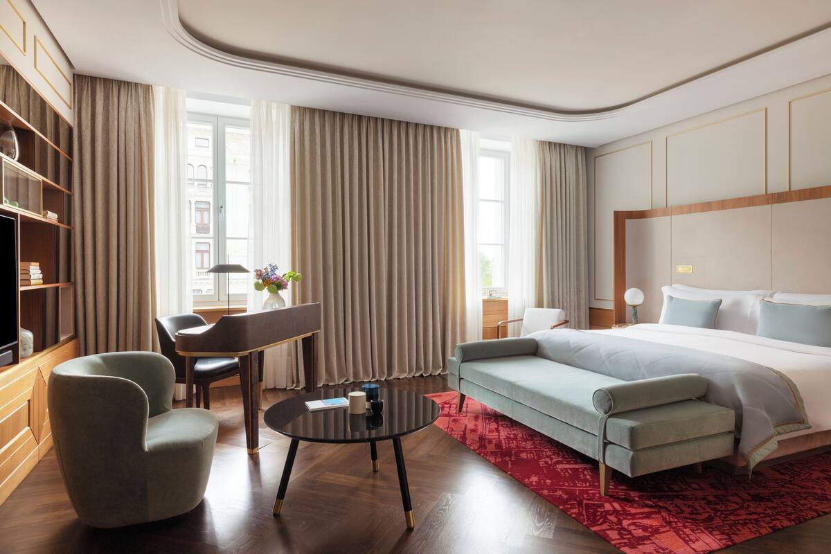A modern hotel room with a large bed, a sofa, a dining table, and a TV.