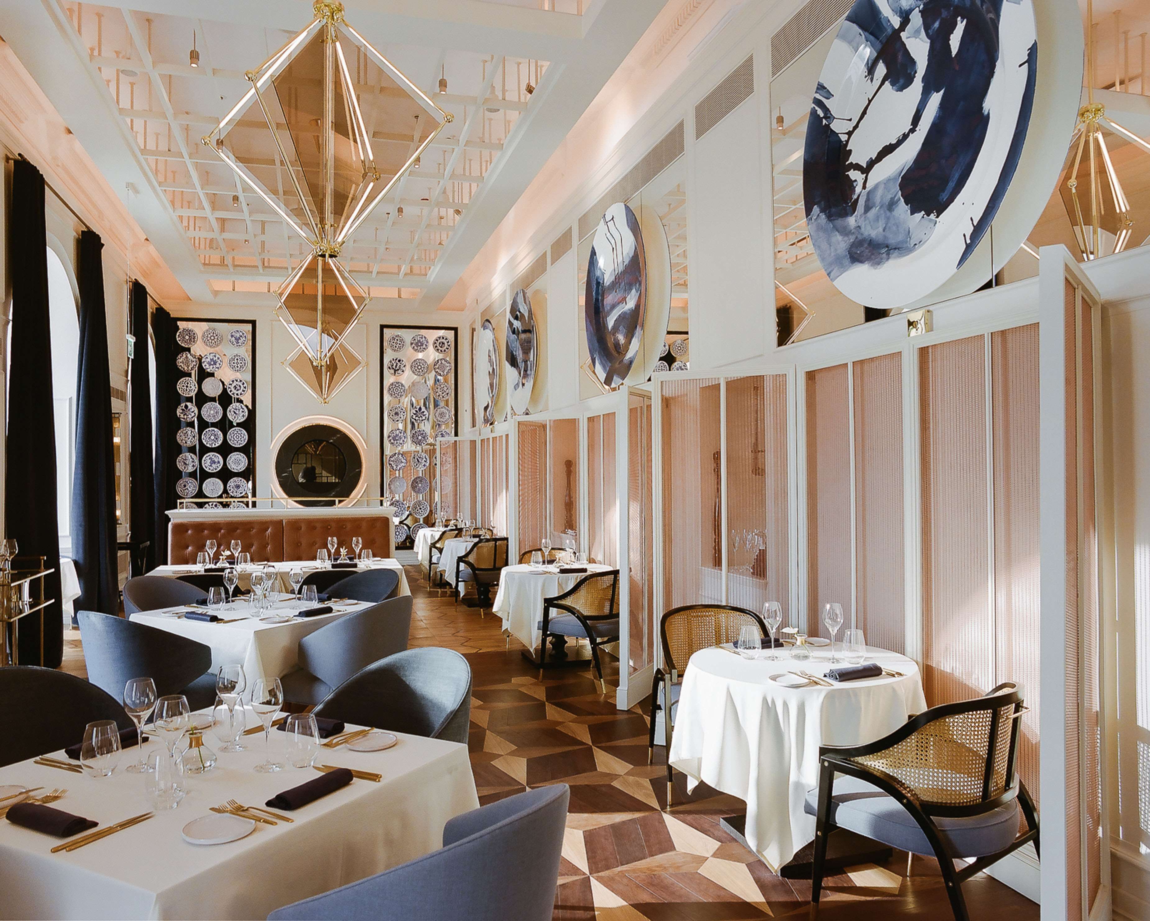A restaurant with multiple tables and chairs, a patterned floor, and decorative ceiling lights.