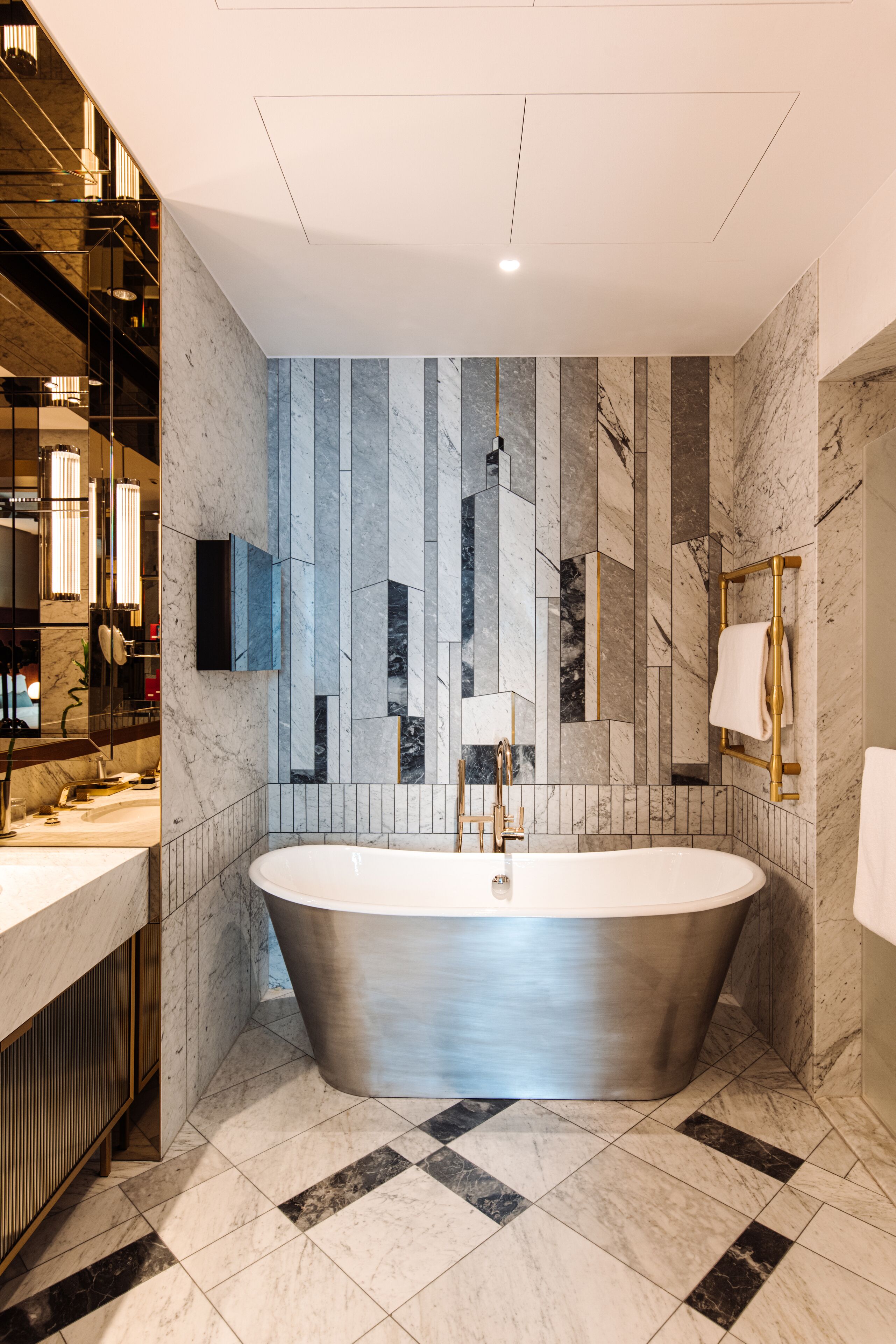 Un baño moderno con una bañera independiente, paredes de mármol y un espejo grande.