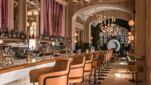 A bar area with a long counter, multiple stools, and a variety of bottles and glasses. - Raffles Europejski Warsaw (Warsaw)