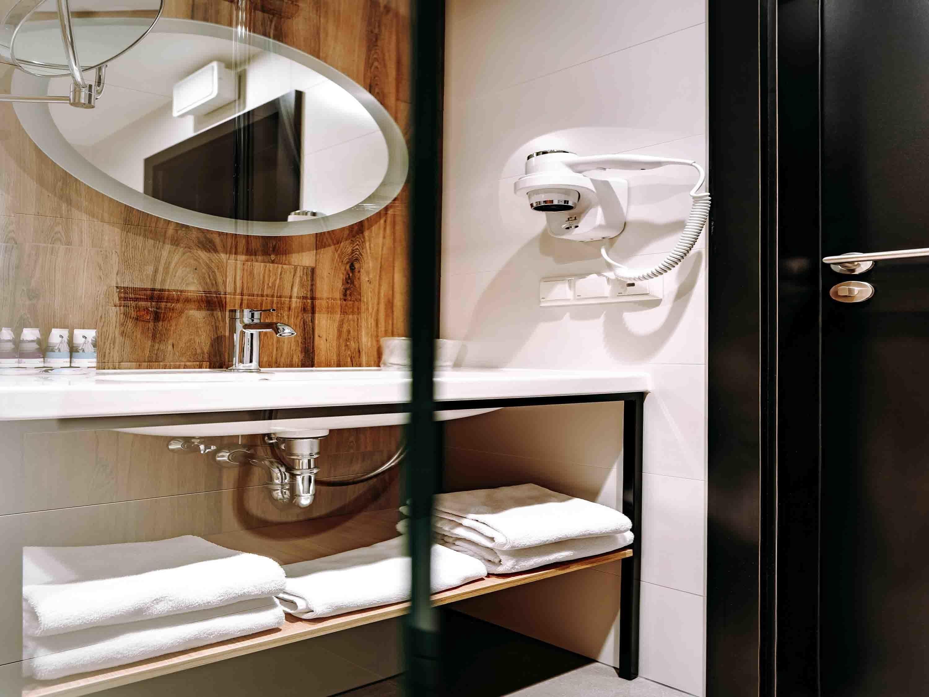 A modern bathroom with a wooden vanity, a round mirror, a hairdryer, and a towel rack.