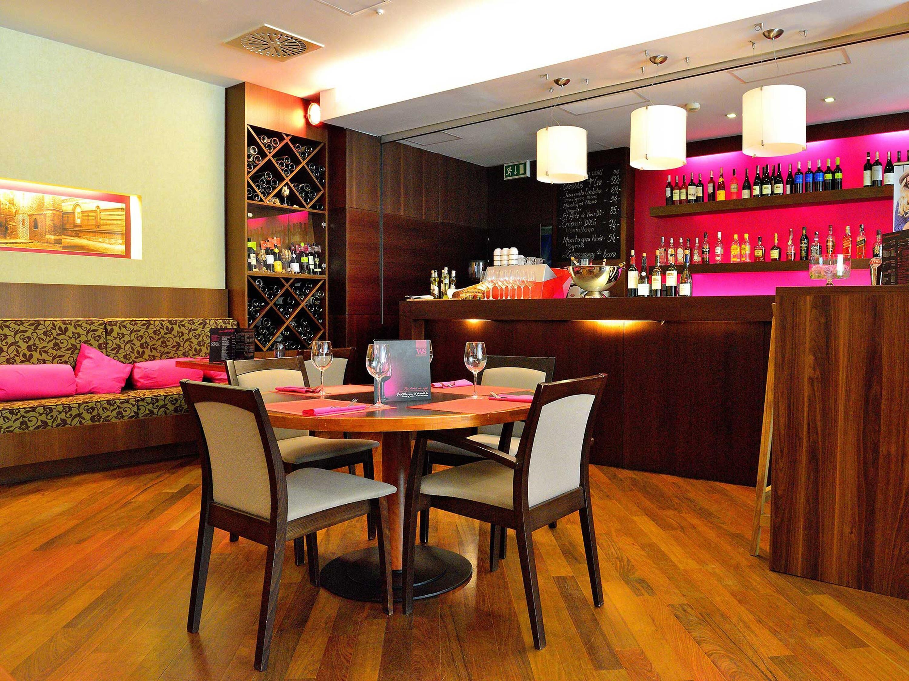 A restaurant interior with a bar, wooden flooring, and a seating area with a sofa and chairs.