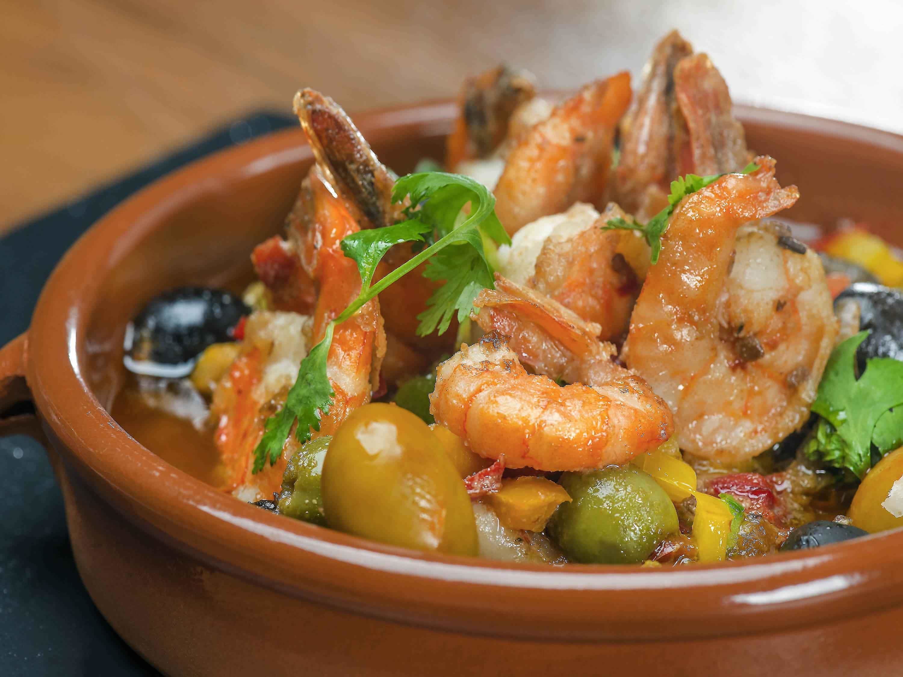 A dish of seafood with shrimp, mussels, and vegetables in a clay pot.