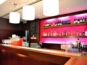 Una zona de bar con mostrador de madera, varias botellas de vino en estantes y una máquina de café.