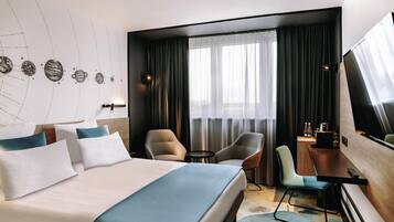 A hotel room with a large bed, two armchairs, a desk, a TV, and a window with curtains.